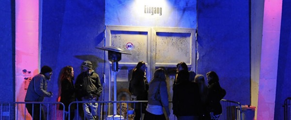 Night queue outside a Berlin club entrance, Eingang sign lit above industrial doors, blue and magenta light on concrete