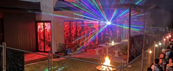 Crowd queuing outside a house party at night, with lasers, smoke and red lighting